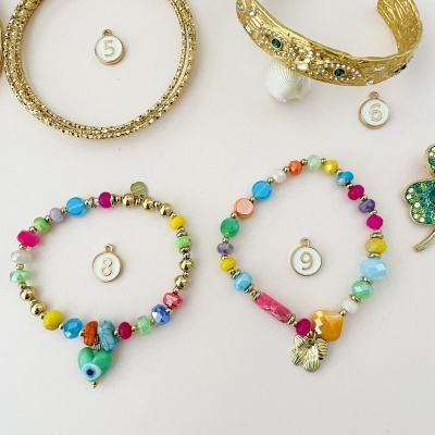 Quatro pulseiras sobre fundo claro, sendo duas douradas e duas coloridas com contas variadas e pendentes.