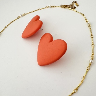 Brincos de coração vermelhos e colar dourado com pérolas em fundo branco