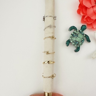 Conjunto de cinco anéis finos e broche de tartaruga verde com pedras, exibidos em fundo branco com flor vermelha.