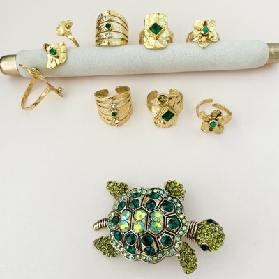 Conjunto de anéis dourados com pedras verdes e broche tartaruga com pedras verdes e azuis