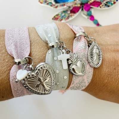 Pulseiras elásticas com pendentes religiosos prateados e broche colorido ao fundo