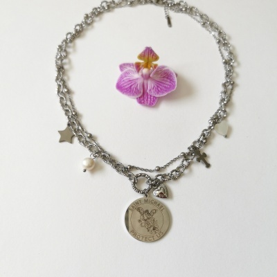 Colar prateado com vários pendentes, incluindo medalha redonda com São Miguel, estrela, cruz, coração e pérola, sobre fundo branco e flor orquídea rosa.