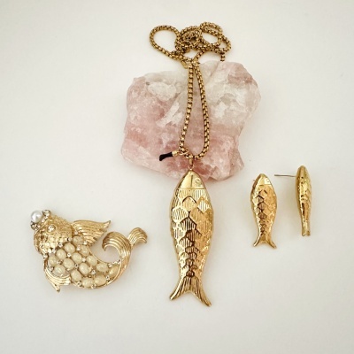 Conjunto de joalharia dourada com pendente, brincos e broche em forma de peixe com pedras e perolas.