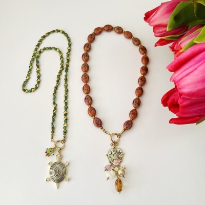 Colares com contas e pendentes em fundo branco, flores rosas ao lado