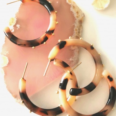 Brincos de argola com padrão de tartaruga e detalhes dourados sobre placa decorativa rosa