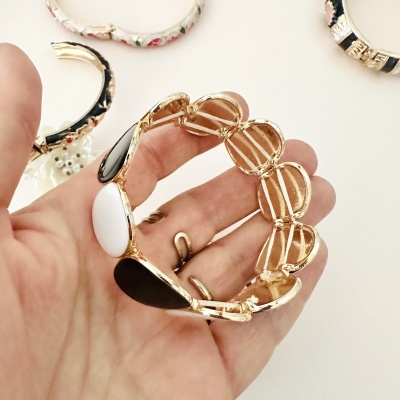 Pulseira dourada com pedras pretas e branca em fundo branco