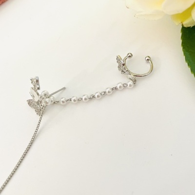 Brinco prateado com pérolas e borboleta sobre fundo branco e flor