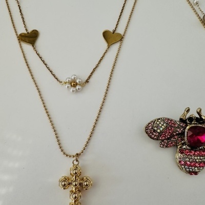 Colares dourados com pingentes de cruz e flor de pérolas, e broche de abelha com cristais coloridos