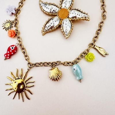 colar dourado com vários pendentes coloridos e broche de flor prateada com centro laranja