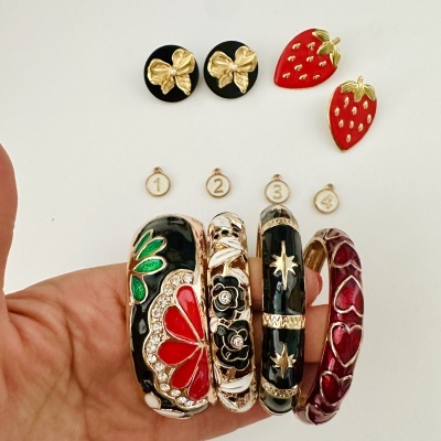 Conjunto de pulseiras esmaltadas e brincos com desenhos florais, corações e morangos em fundo branco
