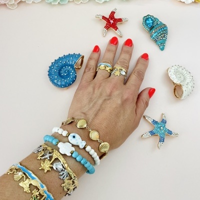 Mão feminina com joias de tema marinho e acessórios coloridos sobre fundo claro