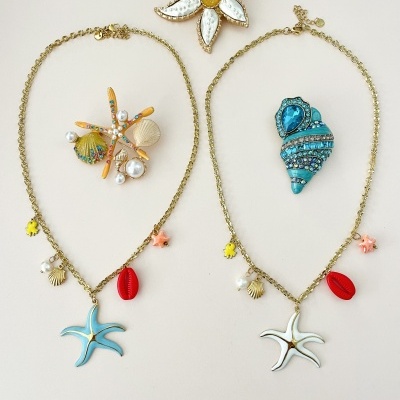Dois colares dourados com pendentes marinhos e dois broches decorativos coloridos