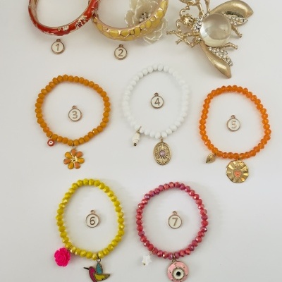 Conjunto de pulseiras coloridas e um broche dourado com pérola em fundo branco