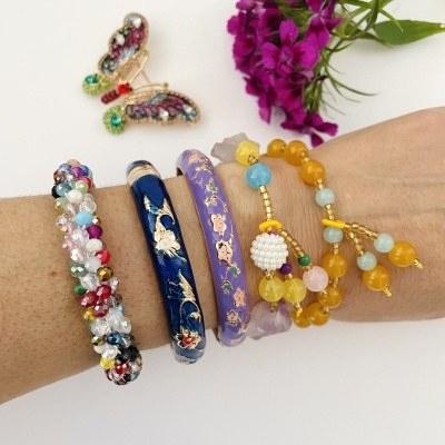 Pulseiras coloridas em braço com borboleta decorativa e flores roxas ao fundo