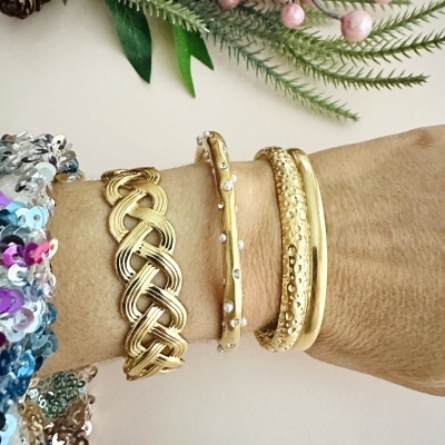 Três pulseiras douradas diferentes num pulso com fundo de folhas e flores