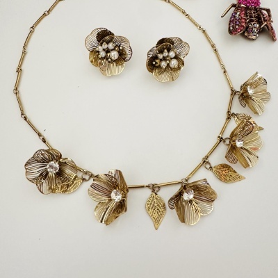 Conjunto de joalharia com flores douradas e pérolas sobre fundo branco