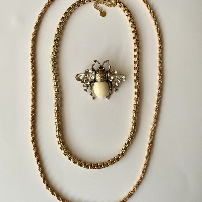 Dois colares dourados e presilha em forma de inseto com corpo perlado em fundo branco