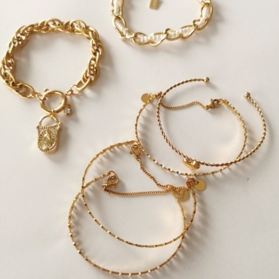 Conjunto de cinco pulseiras douradas com diferentes desenhos sobre fundo branco