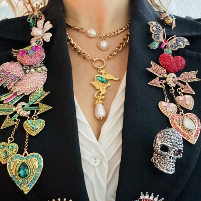 Casaco preto com bordados coloridos e colar dourado com pérola