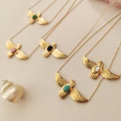 Colares dourados com pedras coloridas em forma de pássaros sobre superfície creme