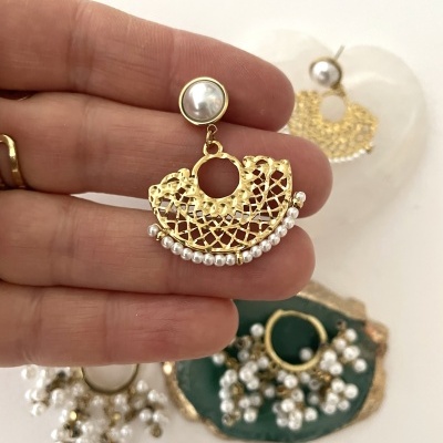 Brinco dourado em leque com pérolas sendo segurado pela mão