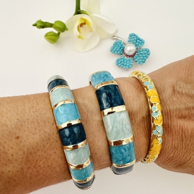 Pulseiras coloridas de tons azuis e amarelos no braço com flor branca e broche azul com pérola