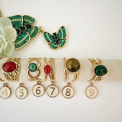 Anéis dourados com pedras coloridas e pendentes numerados, com pendentes em forma de borboleta verde