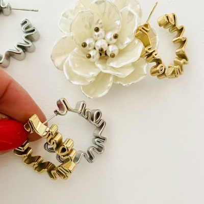 Brincos de aro ondulado dourado e prateado e brinco flor branco com pérolas sobre fundo branco