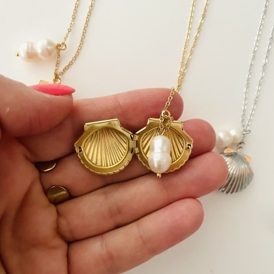 Colar com pendente de concha dourada e pérola, sendo mostrado na mão, com dois colares semelhantes ao fundo.