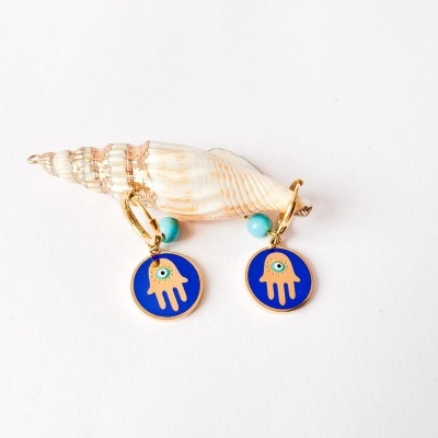 brincos com símbolo de mão hamsá azul e amarelo com conta turquesa sobre concha marinha