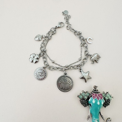 Pulseira prateada com pendentes variados e objeto colorido ao lado