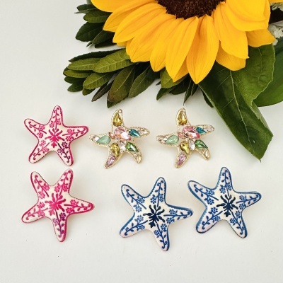 Broches estrela do mar com padrões rosa, azul e pedras coloridas com girassol e folhas verdes ao fundo