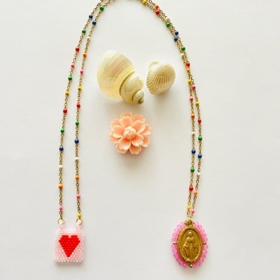 Colar com contas coloridas, pingentes em forma de saco com coração e oval dourado, conchas e flor cor de pêssego sobre fundo branco