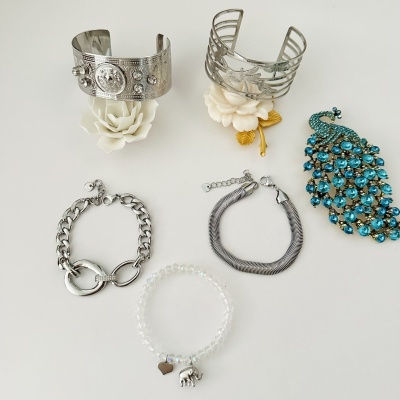 Bijuterias com braceletes, pulseiras e broche em pavão azul sobre fundo branco