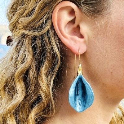 Brinco pendente azul em forma de folha com acabamento dourado na orelha de mulher