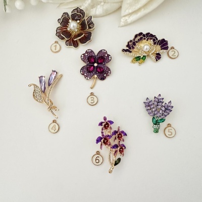 Seis broches florais decorativos com pedras e pérolas em fundo branco.