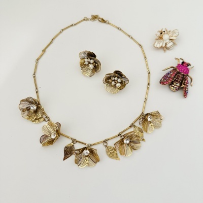 Conjunto de bijuterias douradas com colar floral, brincos com pérolas e broches em forma de abelha