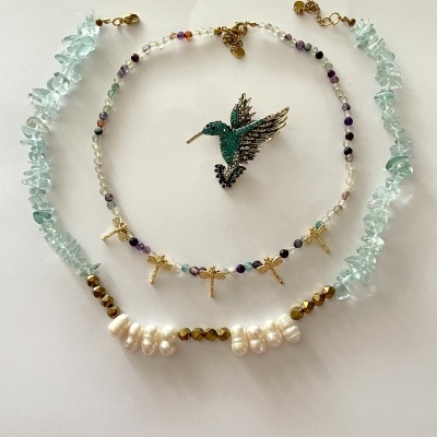 Colares e broche com pedras coloridas e pérolas sobre fundo branco.