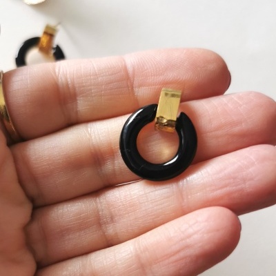 Brinco preto circular com fecho dourado segurado por mão