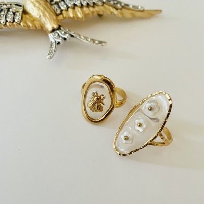 Dois anéis dourados com detalhes de abelha e pérolas, ao lado de figura de pássaro dourado