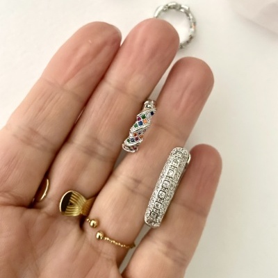 Anéis finos em prata com pedras coloridas e brancas e anel em ouro com design ondulado na mão