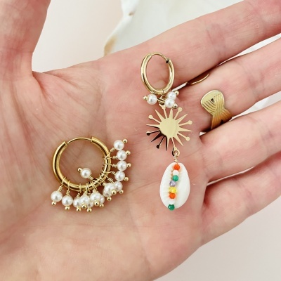 Par de brincos dourados com pérolas e concha colorida numa mão