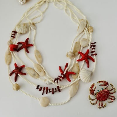 Colar com contas brancas, pedras bege, conchas e estrelas do mar vermelhas, e broche de caranguejo vermelho