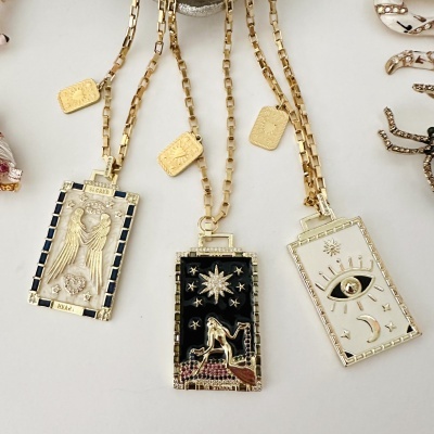 Três colares dourados com pendentes retangulares decorados e detalhes místicos