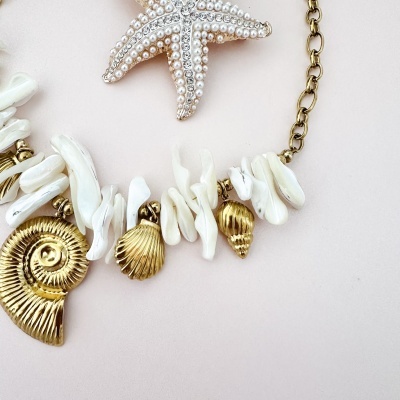 Colar com conchas, pedras brancas e pendentes dourados em fundo rosa claro