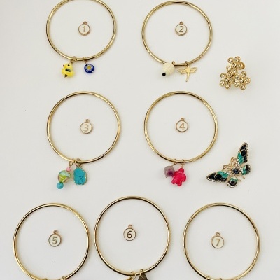 Sete pulseiras douradas numeradas com pendentes variados sobre fundo branco