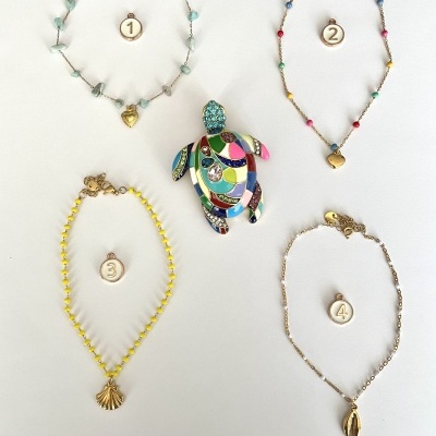 Quatro pulseiras com pendentes e uma tartaruga colorida ao centro sobre fundo branco.