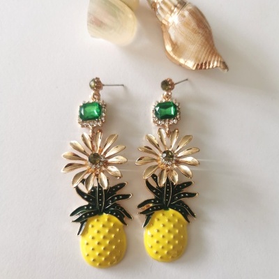 Brincos coloridos em forma de abacaxi com pedra verde e conchas no fundo