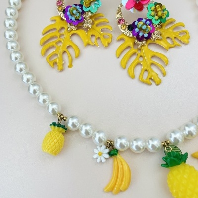 Colar de pérolas com pendentes de frutas e brincos coloridos em fundo branco