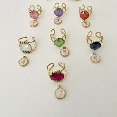 Anéis com pedras coloridas e etiquetas numeradas em fundo branco